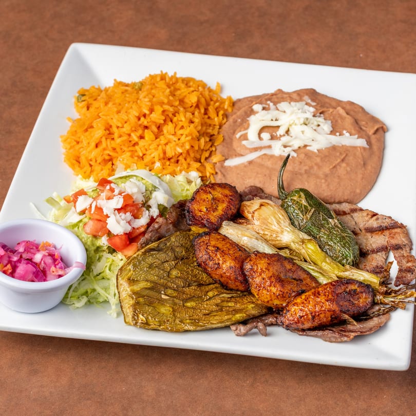 Mexican platter with rice, beans, grilled meat, plantains, nopales, and a side of pickled onions.
