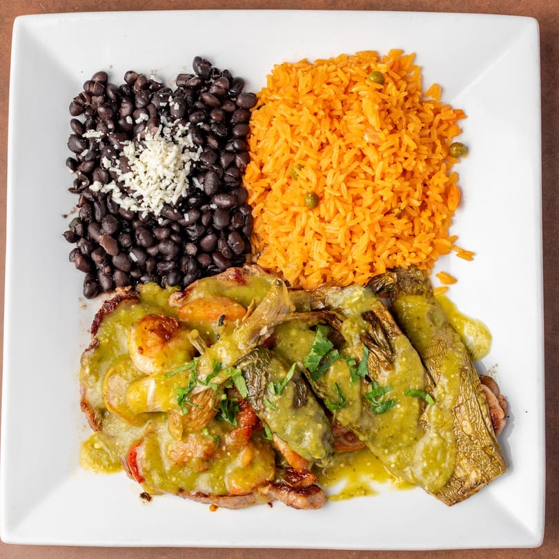 A Mexican dish with green chile stew, shrimp, rice, and black beans on a white plate.