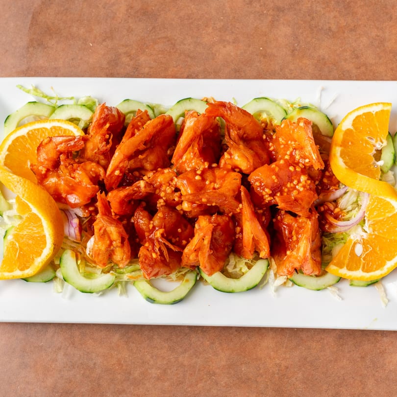 Spicy orange shrimp with cucumber slices, shredded lettuce, and orange wedges on a white plate.